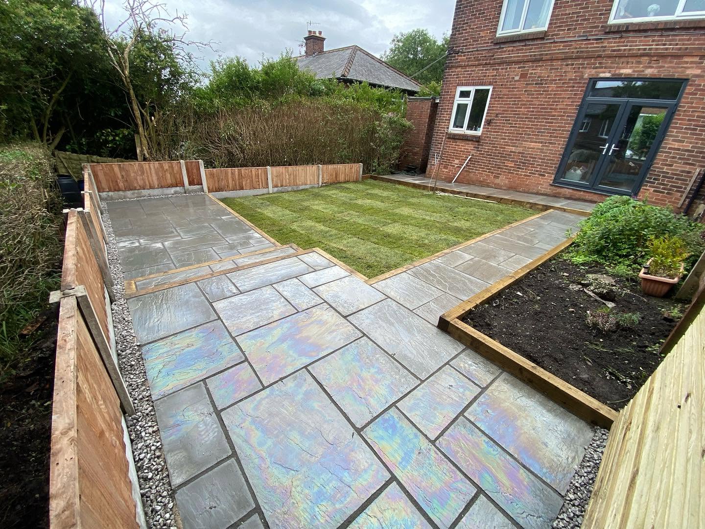 A finished Indian sandstone patio with a freshly turfed lawn in a Greater Manchester garden